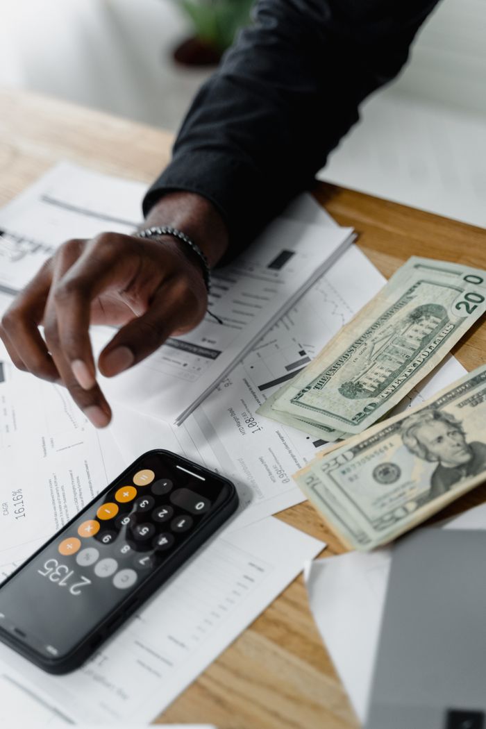 services-03 A person calculating expenses using a smartphone and counting cash bills on a wooden table.